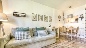 A living room with a sofa, a dining table, chairs, a lamp, and wall art.