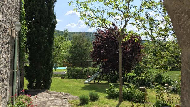 A stone pathway leading to a garden with a playground, a tall tree, and a view of a distant landscape.