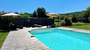 A swimming pool with a wooden deck, lounge chairs, and umbrellas.