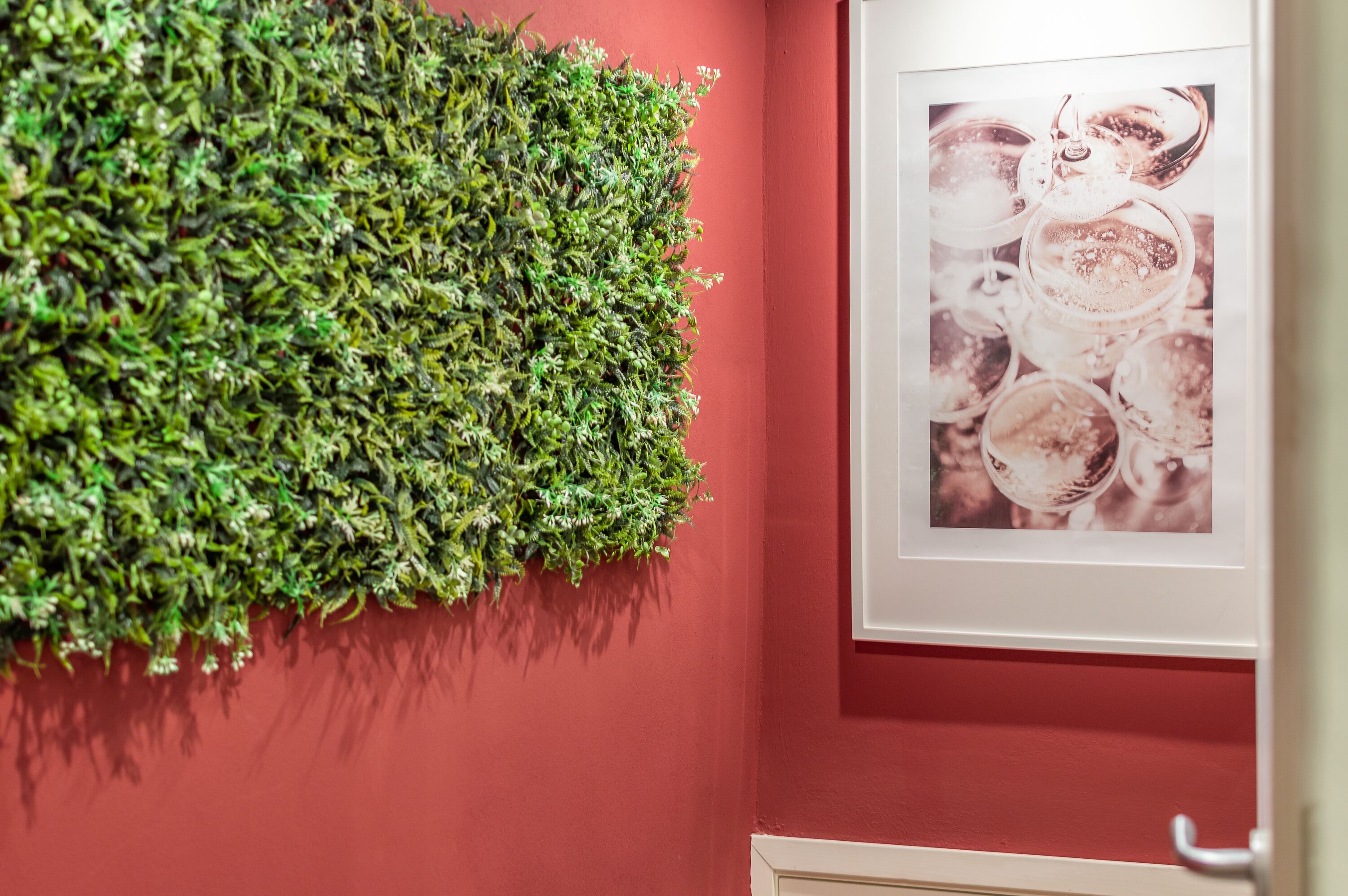 A wall with a green vertical garden and a framed photograph of drinks.