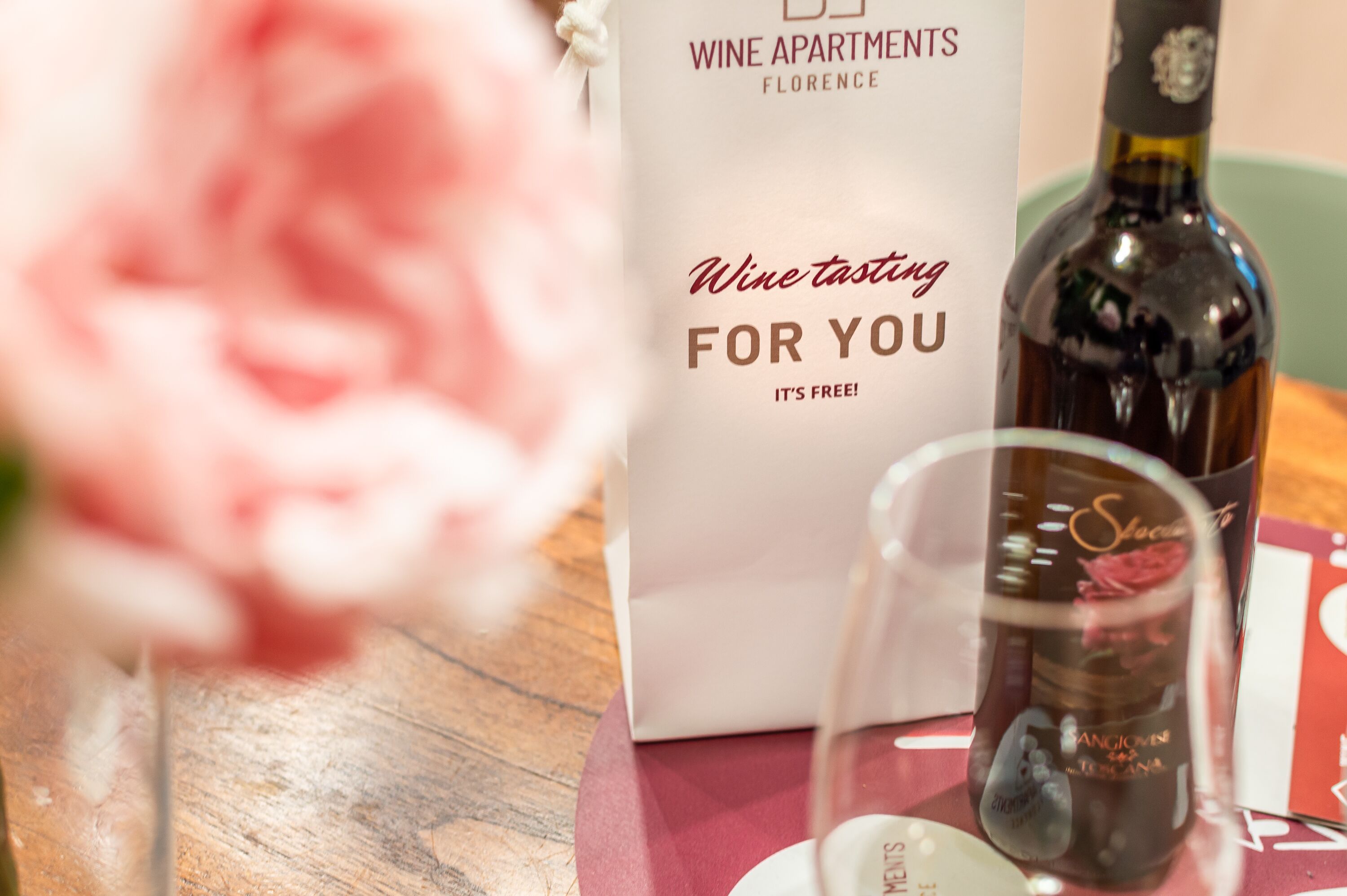 A wine tasting event setup with a bottle of wine, a glass, and a sign that reads "Wine tasting for you, it's free!"