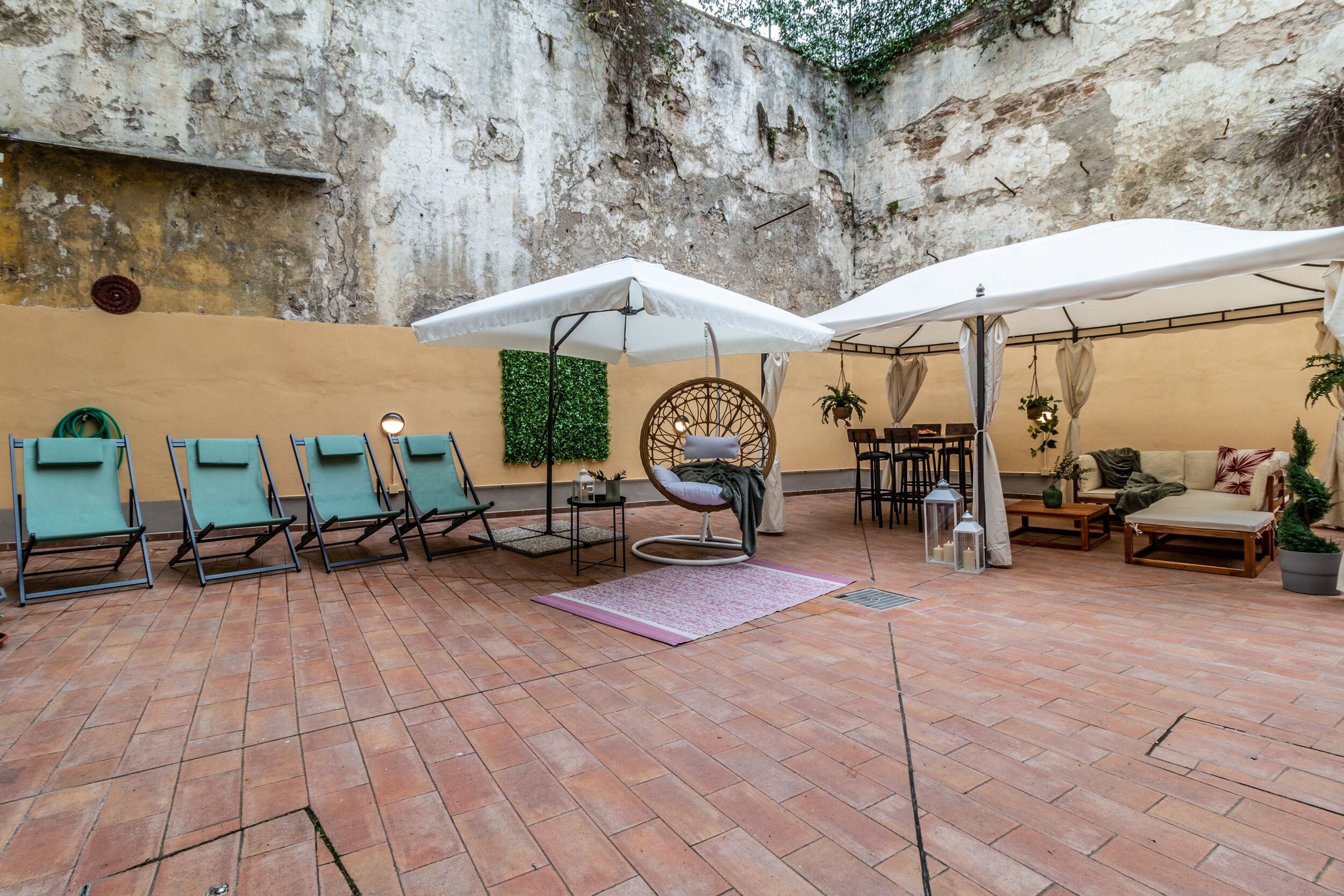 An outdoor patio with tiled flooring, several lounge chairs, a hanging chair, and a seating area with a table and chairs.