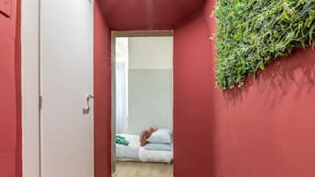 Un corridoio stretto con una parete rossa, una porta bianca e un letto con coperta e cuscini verdi.
