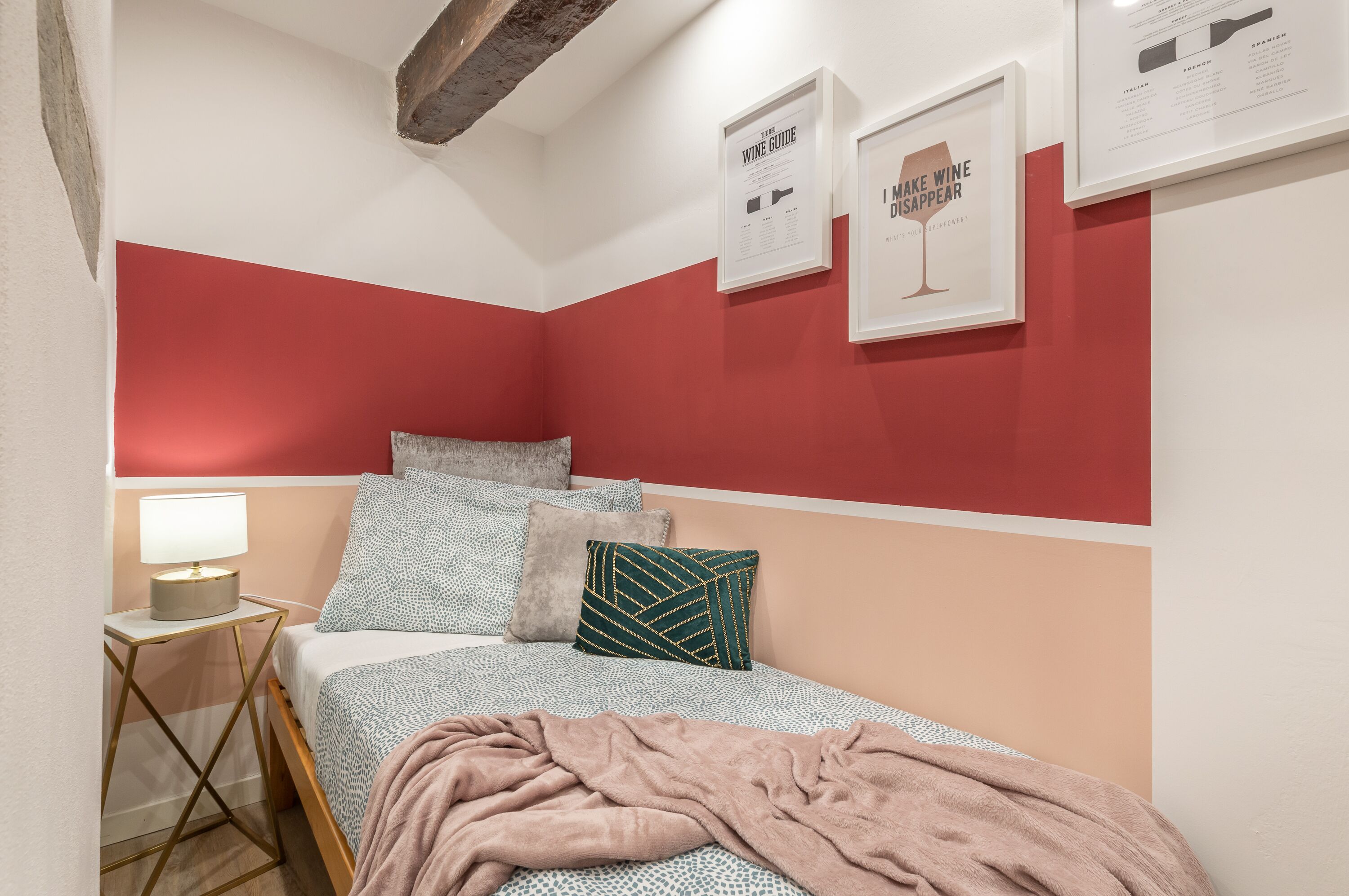 Ein Schlafzimmer mit Bett, Kissen, Nachttisch mit Lampe und gerahmten Postern an der Wand.