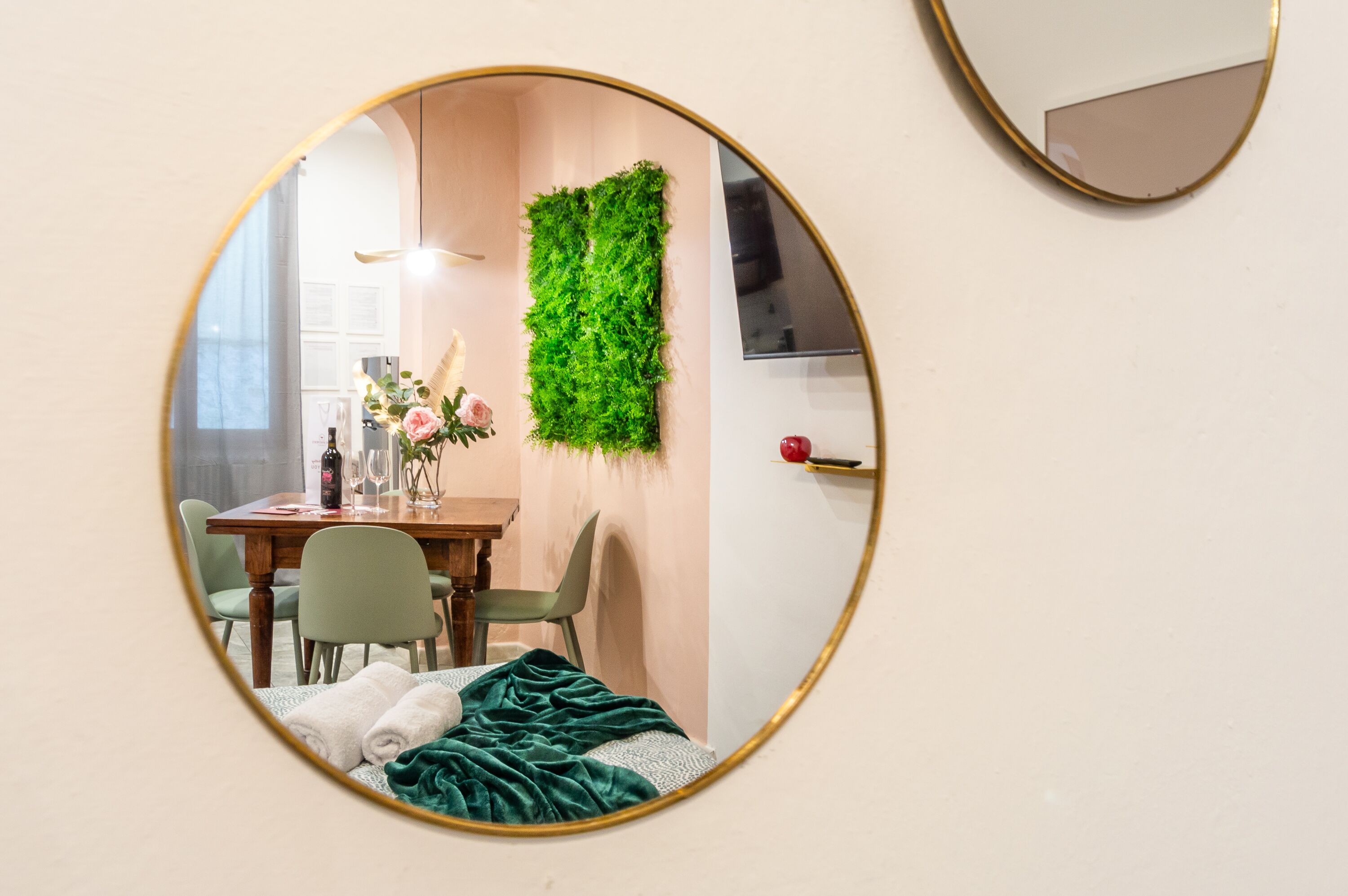 Una stanza con un letto, un tavolo da pranzo con sedie, uno specchio e una decorazione verde al muro.