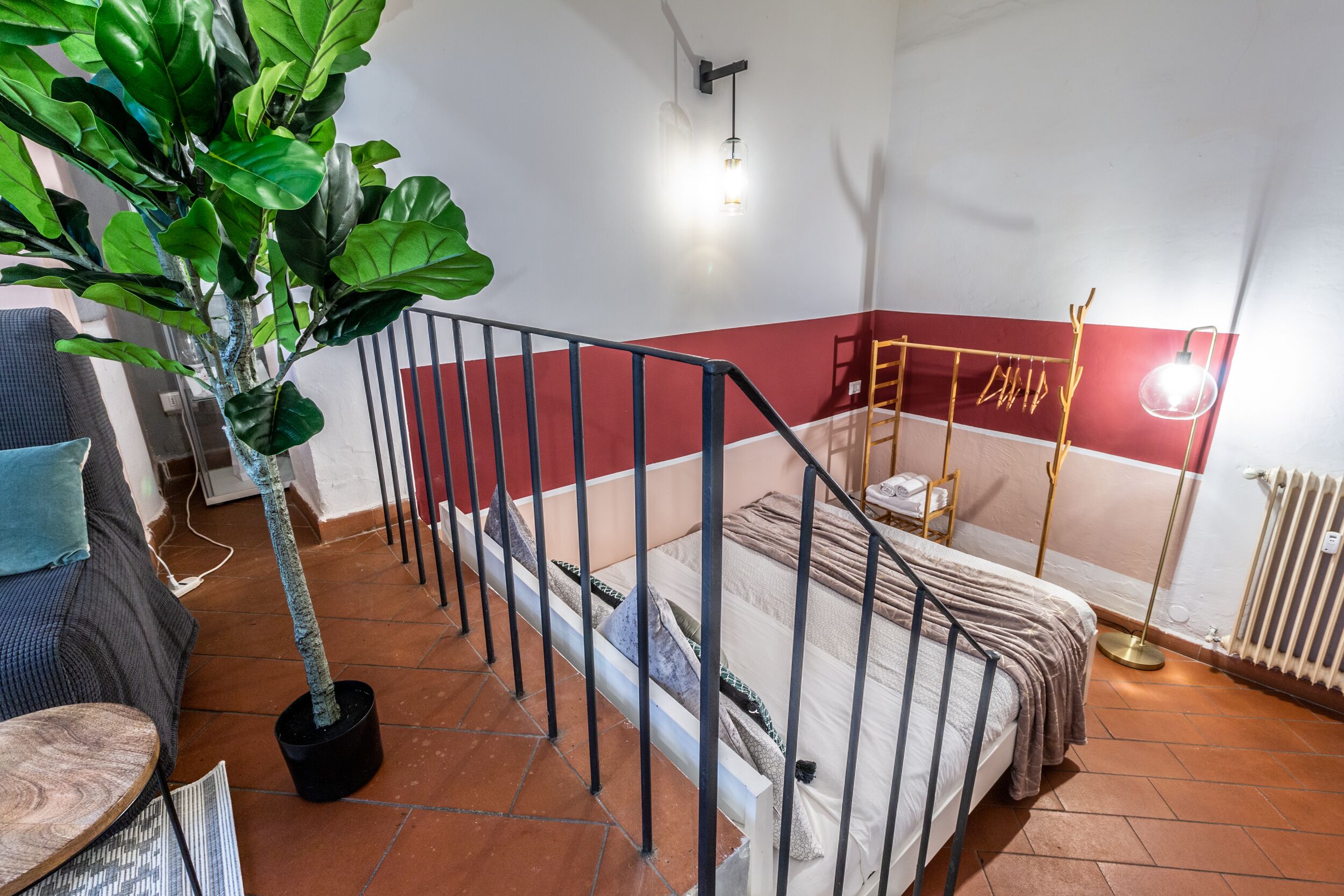 A bedroom with a bed, a potted plant, a radiator, and a wall-mounted light fixture.