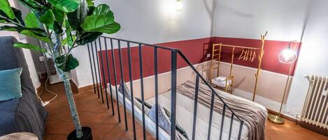 A bedroom with a bed, a potted plant, a radiator, and a wall-mounted light fixture.