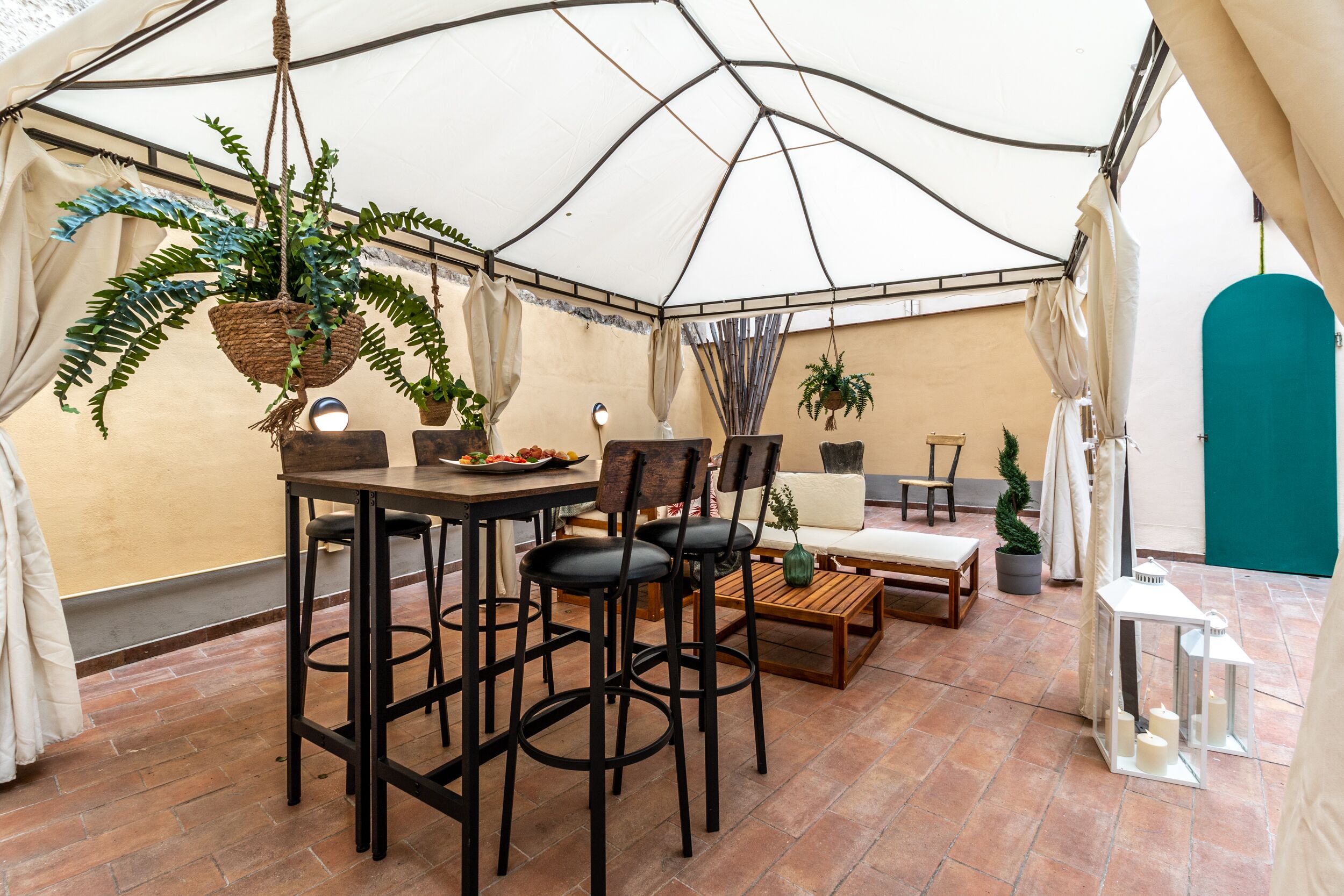 Un área de comedor con carpas, una mesa, sillas y plantas colgantes.