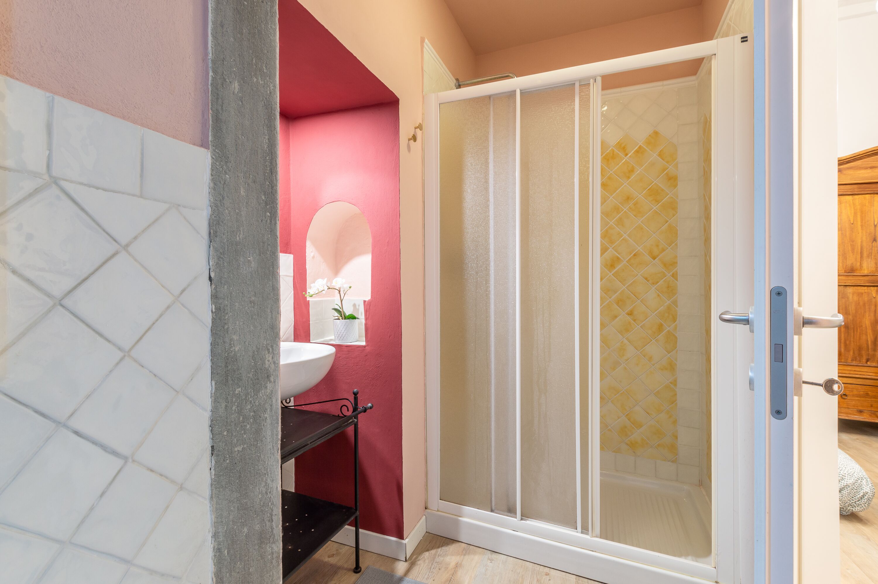 A bathroom with a white sink, a mirror, a potted plant, and a shower with a glass door.