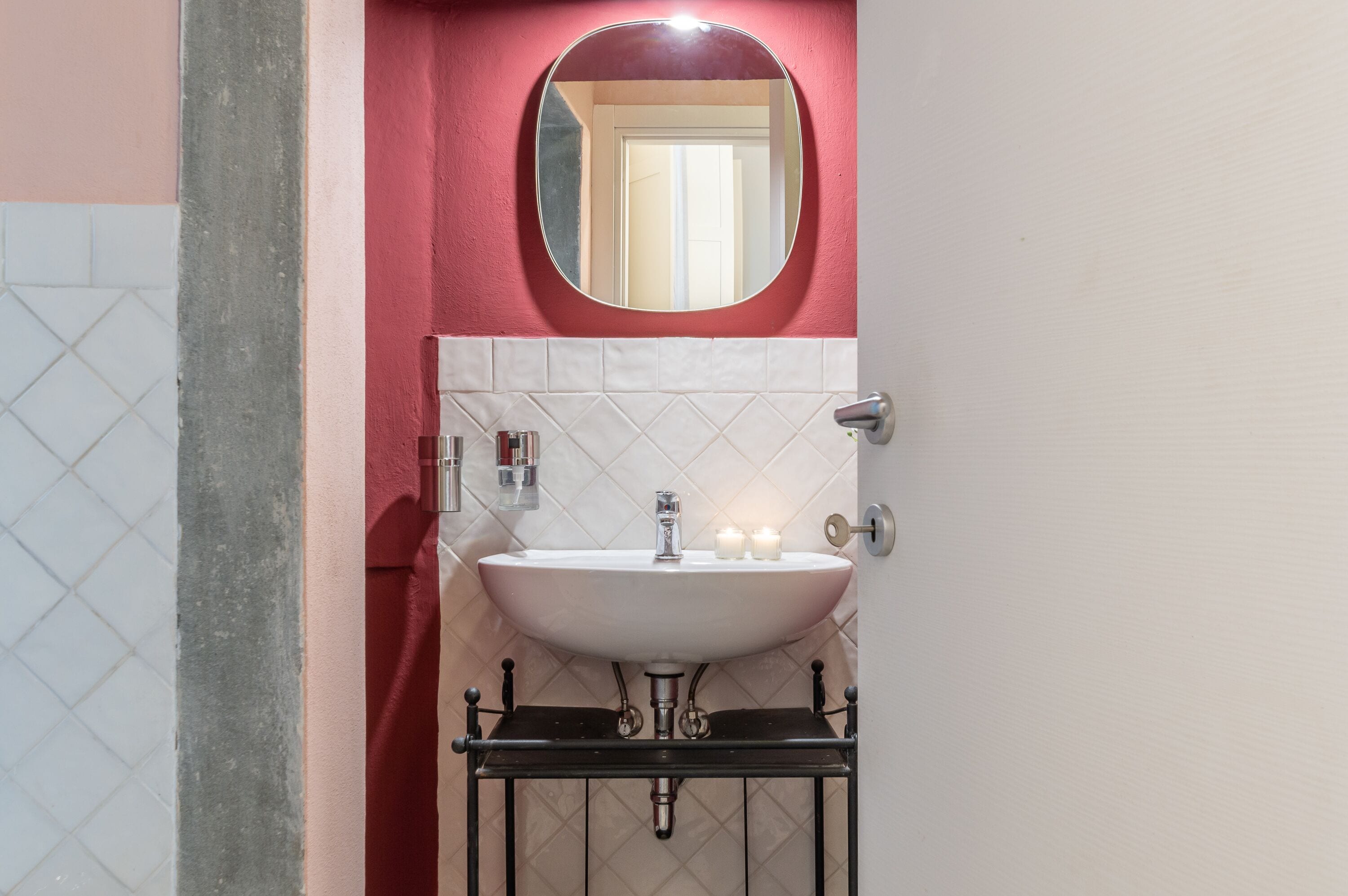 Un baño con un lavamanos blanco, un espejo redondo y una pared roja.