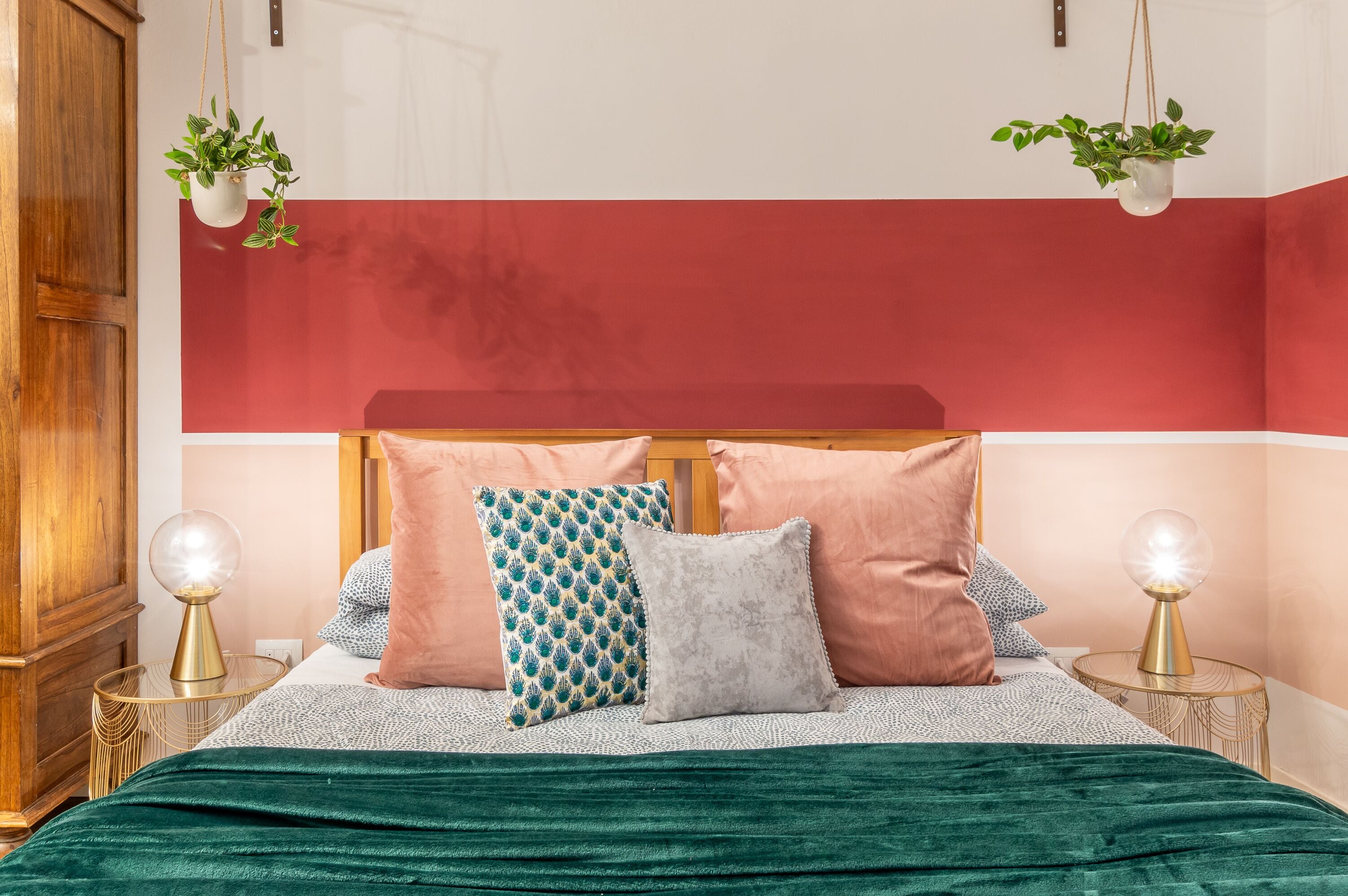 Uma cama com um cobertor verde, duas mesas de cabeceira com luminárias e uma parede vermelha e branca.