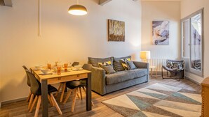 Een eethoek met een houten tafel en stoelen, een grijze bank en een vloerkleed met een patroon.