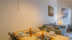 Een eetgedeelte met een houten tafel gedekt voor twee personen, een bank en een schilderij aan de muur.