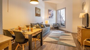Een moderne woonkamer met een eethoek, een bank, een televisie en een groot raam.