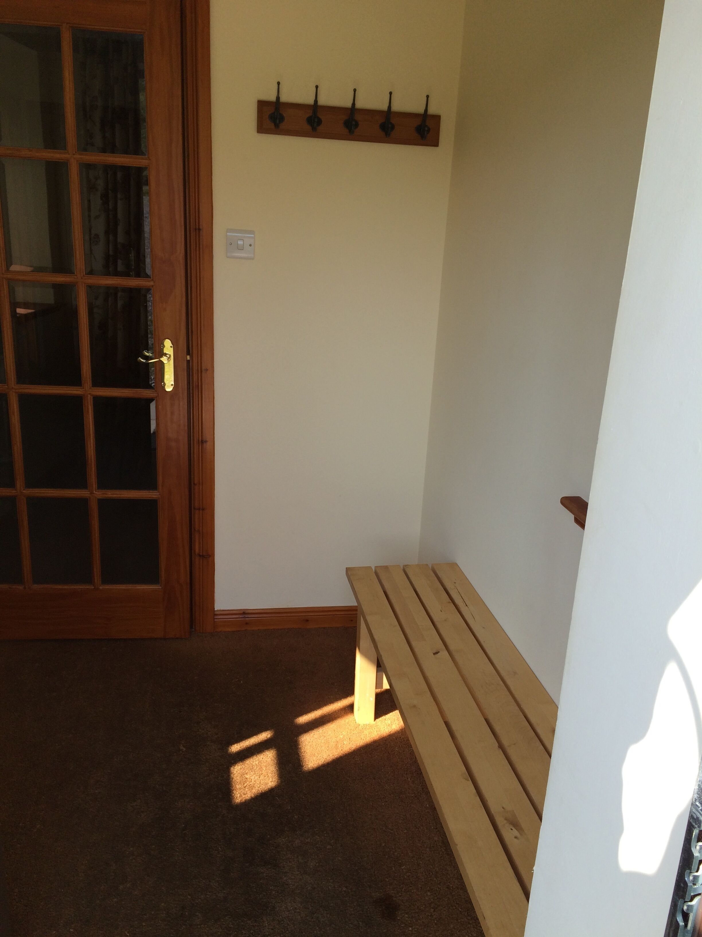 Ein Zimmer mit einer Holzbank, einer Glastür und einem an der Wand befestigten Kleiderhaken.