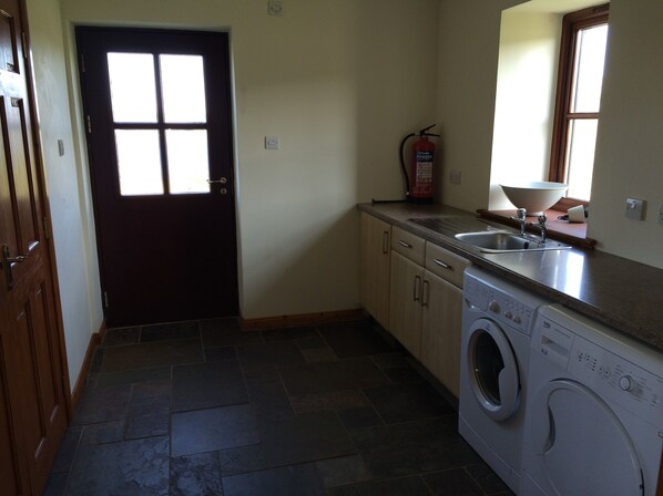 A compact kitchen with a washing machine, a fire extinguisher, and a window.