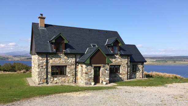 A stone house with a dark roof, a chimney, and a view of a lake. - In the heart of the Highlands located on a Private Sporting Estate (Lairg)