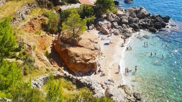 A coastal area with rocky terrain, clear blue sea, and a small boat in the distance.