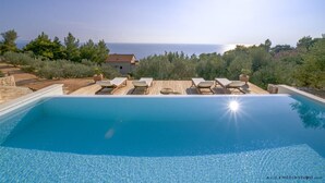 A swimming pool with lounge chairs, a view of the sea, and a house in the background.