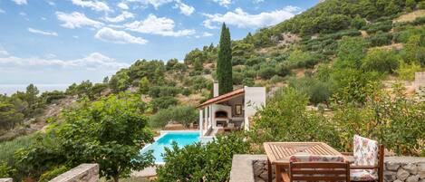 Una villa con piscina, mobiliario exterior y vistas a las colinas circundantes.