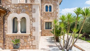 A stone building with arched windows and a stone pathway leading to a palm tree garden. - PREMIUM: GRAND AND ELEGANT VILLA (Sa pobla)