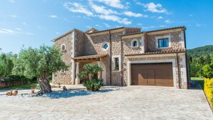 A stone house with a garage, surrounded by a garden with trees and plants. - PREMIUM: GRAND AND ELEGANT VILLA (Sa pobla)