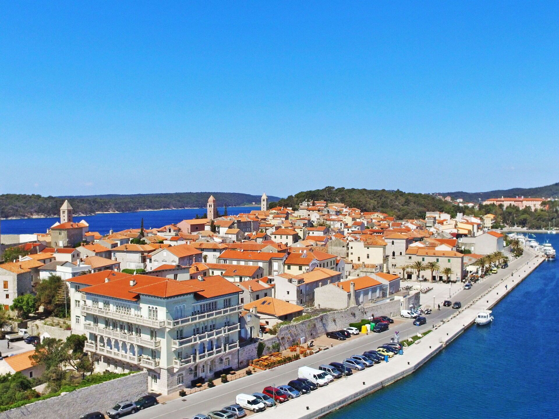 Un pueblo costero con edificios históricos, un puerto deportivo y una carretera frente al mar.