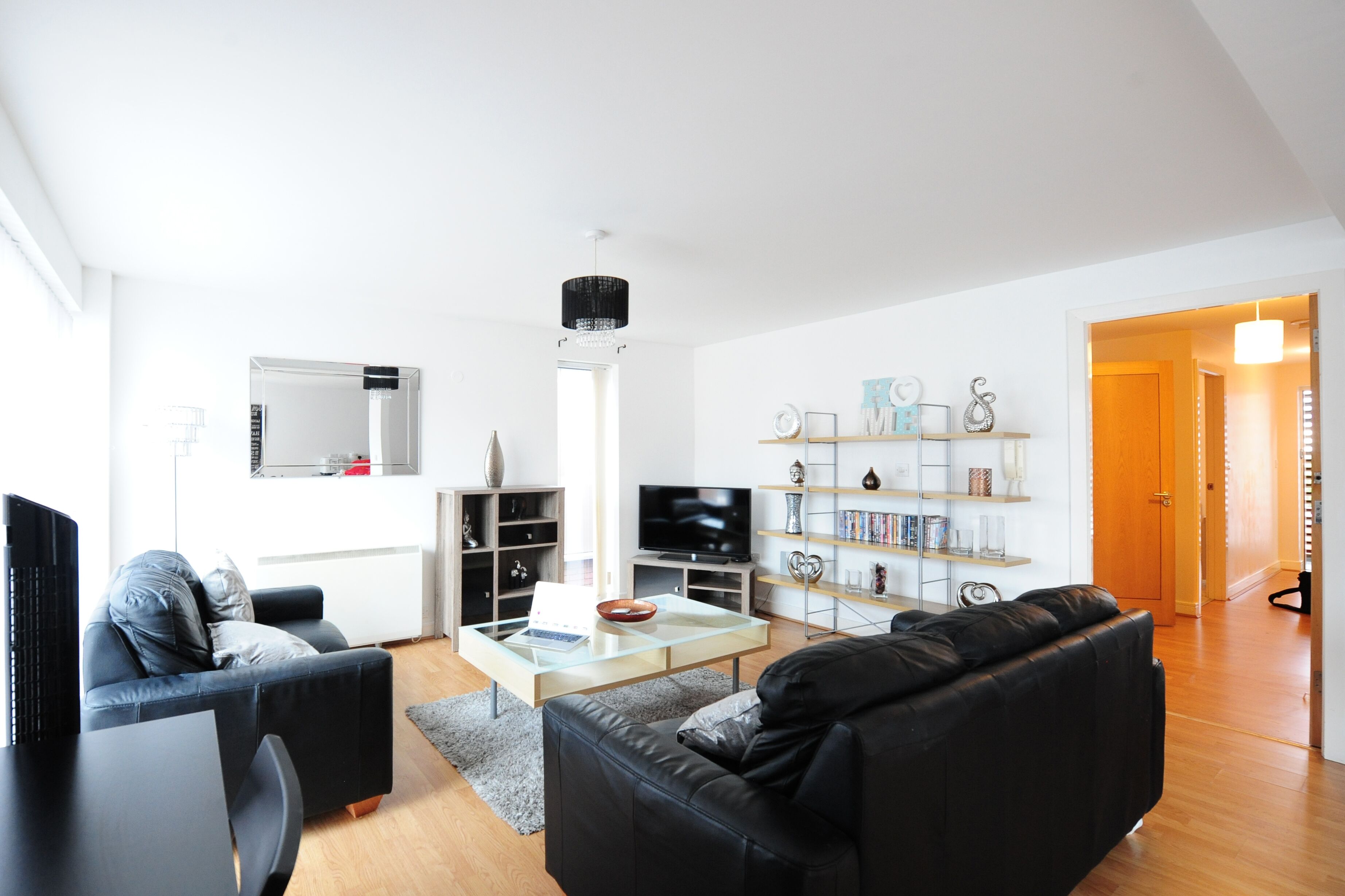 Ein modernes Wohnzimmer mit einer schwarzen Ledersofa, einem Glastisch, einem Flachbildfernseher und einem Bücherregal.