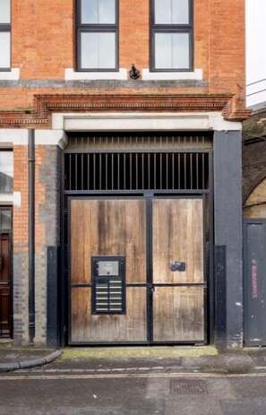 A large, wooden double door with a metal gate, set in a brick building with a white trim and a small window above the door.