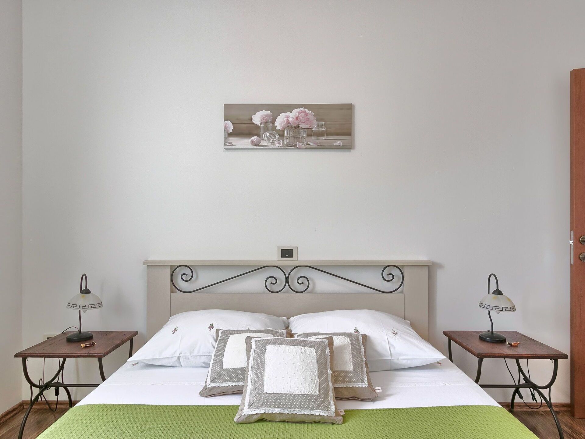 Une chambre à coucher bien rangée, avec un lit, deux tables de chevet, une horloge murale et un objet décoratif placé au-dessus du lit.