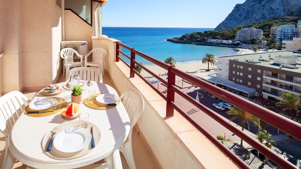 Un balcon avec une table dressée pour le dîner, offrant une vue sur une plage et les bâtiments qui bordent la côte.
