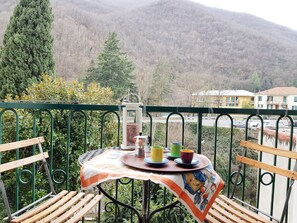 A balcony with a table set for two, a metal railing, and a view of a mountain and buildings in the background.
