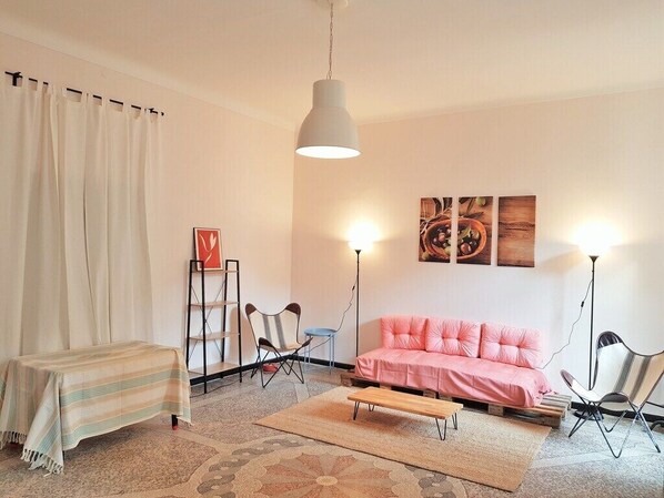 A living room with a pink sofa, a wooden coffee table, a striped tablecloth-covered table, and two floor lamps.