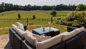 A wicker sofa set with cushions, a glass-top table, and a vase with flowers.
