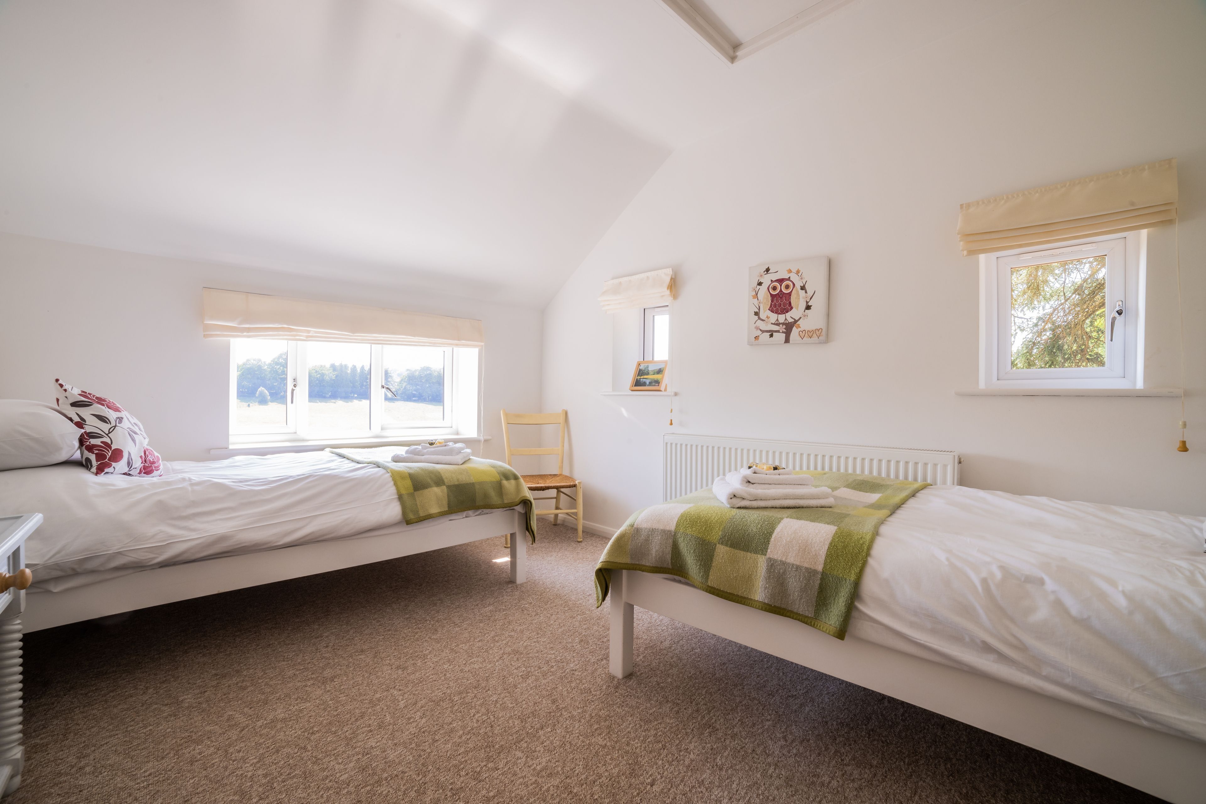 A bedroom with two single beds, a chair, a radiator, and a window with a view.