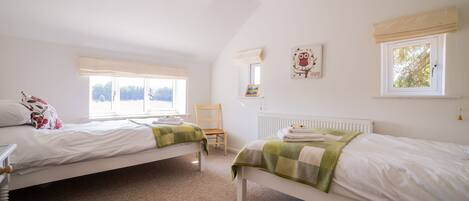 A bedroom with two single beds, a chair, a radiator, and a window with a view.