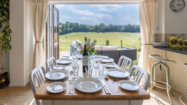 A dining table set for six with a view of a green field through a glass door.