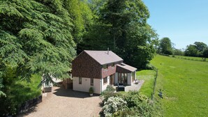A two-story house with a gravel driveway, surrounded by lush greenery and trees.