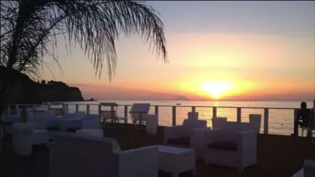 Un espace de détente aménagé sur la plage, avec des chaises longues blanches et une vue sur le coucher de soleil sur l’océan.