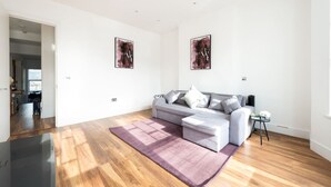 Ein geräumiges Wohnzimmer mit grauem Sofa, einem kleinen Beistelltisch und zwei abstrakten Bildern an den Wänden.