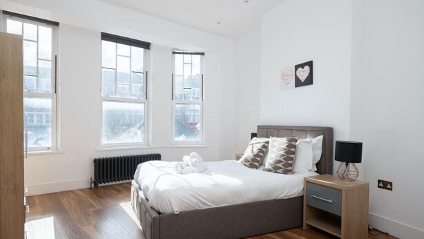 Ein Schlafzimmer mit einem großen Bett, einem Nachttisch, einer Heizung und zwei Fenstern.
