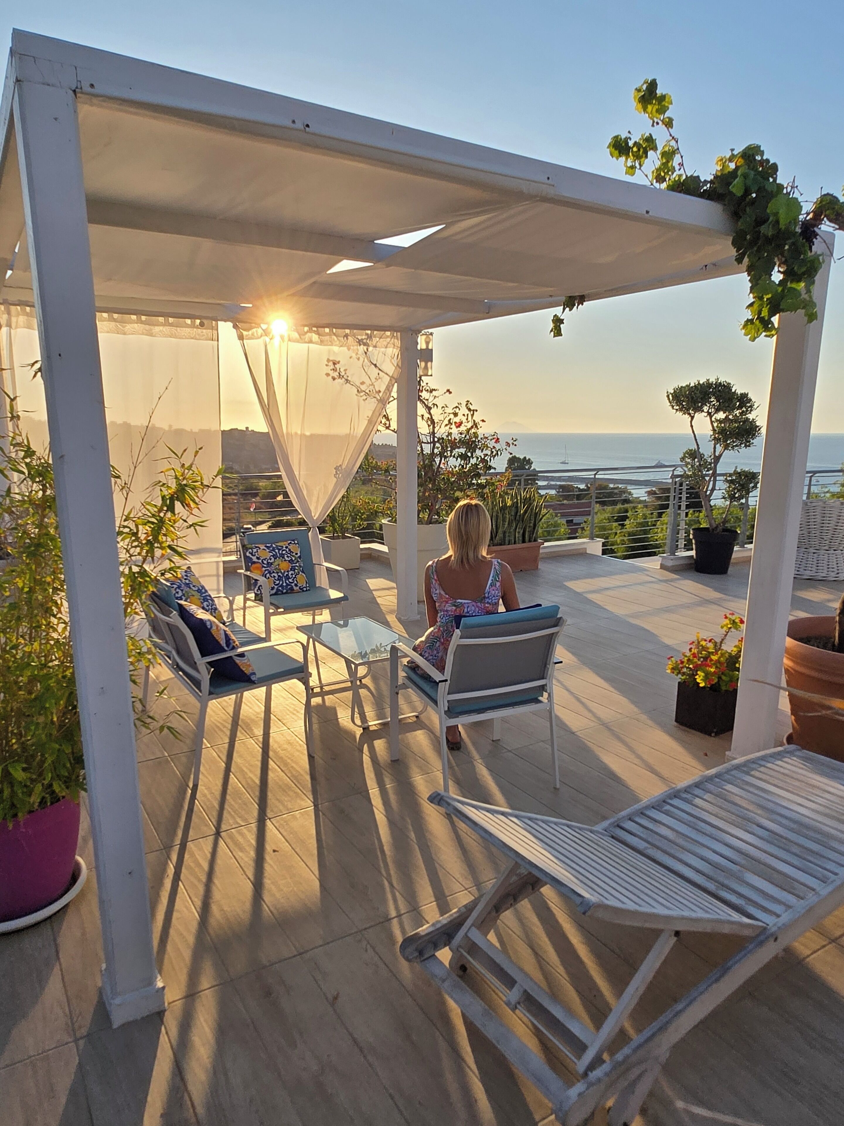 A covered outdoor seating area with chairs and tables, overlooking a scenic view of the sea.