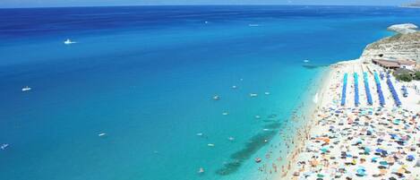 A beach with clear blue water, a sandy shore, and numerous umbrellas.