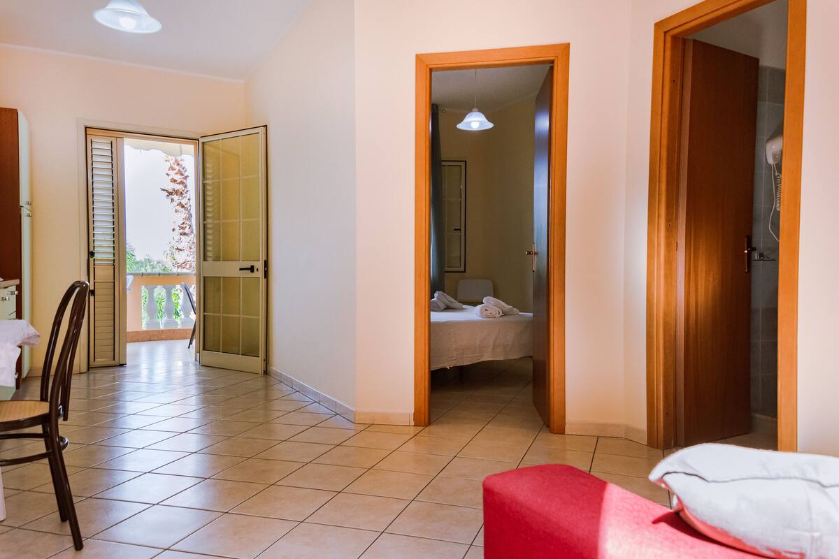 A hotel room with a bed, a chair, a table, and a balcony.
