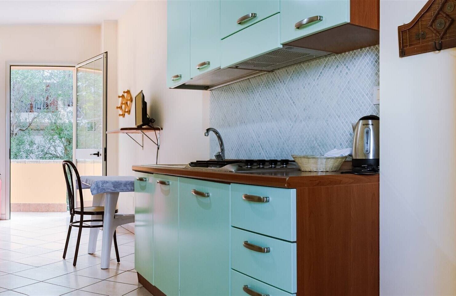 A kitchen with teal cabinets, a wooden countertop, a gas stove, and a kettle.