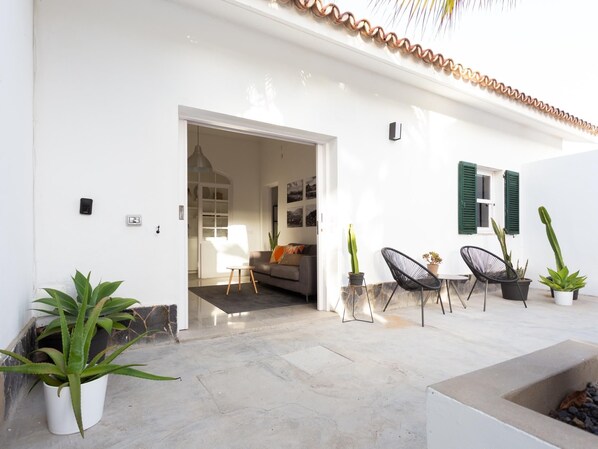 A spacious patio with a modern outdoor seating area, a white wall with a door leading to a living room, and several potted plants. - VILLA MARIA - CASERÍO DE GUAZA (Arona)