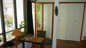 A room with a wooden table and chairs, a lamp, a plant, and a view of the outside through a window. - Paris 20 Pere Lachaise: VERY QUIET STUDIO WITH A TERRACE (Paris)