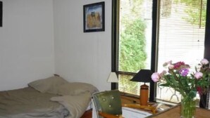 A room with a bed, a chair, a table with a lamp, and a vase with flowers. - Paris 20 Pere Lachaise: VERY QUIET STUDIO WITH A TERRACE (Paris)