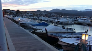 A marina with boats docked, a wooden walkway, and a cityscape in the background.