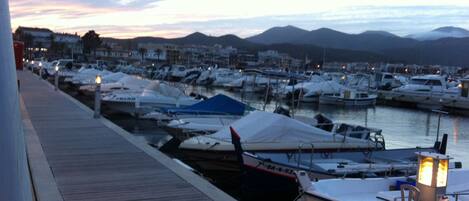 A marina with boats docked, a wooden walkway, and a cityscape in the background.